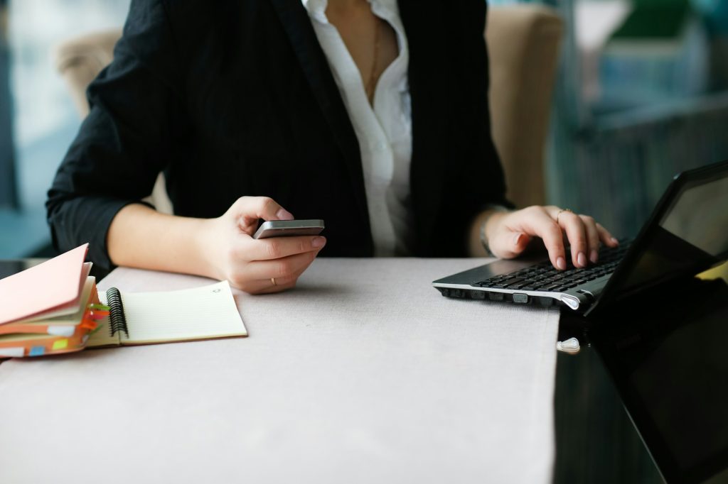 Woman in business suit working with smartphone and laptop